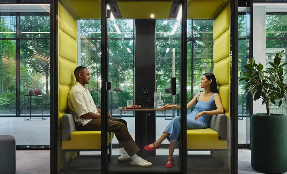 Two people talking inside a Thinkspace acoustic pod surrounded by greenery